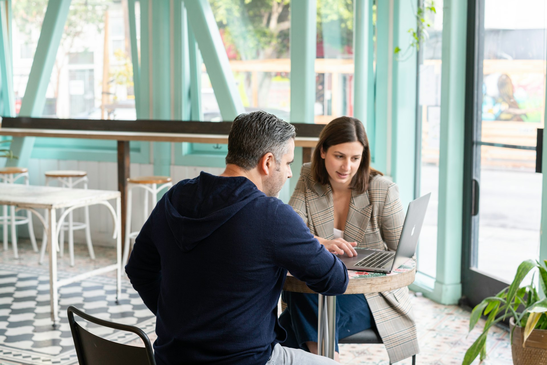 Two professionals collaborating on a laptop in a cozy café with natural light and a modern interior.